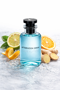 Blue perfume bottle labeled 'Afternoon Swim' by Louis Vuitton with citrus fruits and ginger on a marble surface.